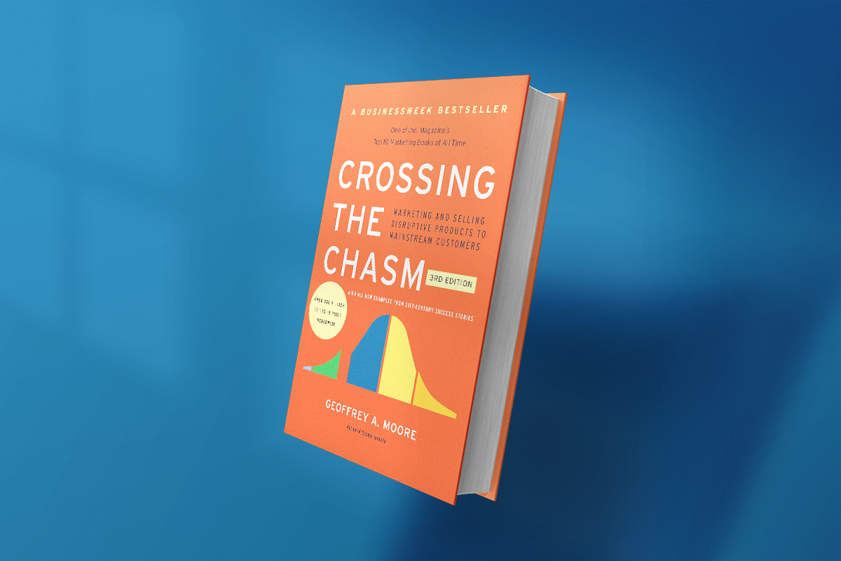 The book Crossing the Chasm by Geoffrey A. Moore, with a bold orange cover and a bell curve graphic, offers marketing insights on how to move disruptive products from early adopters to the mainstream market.